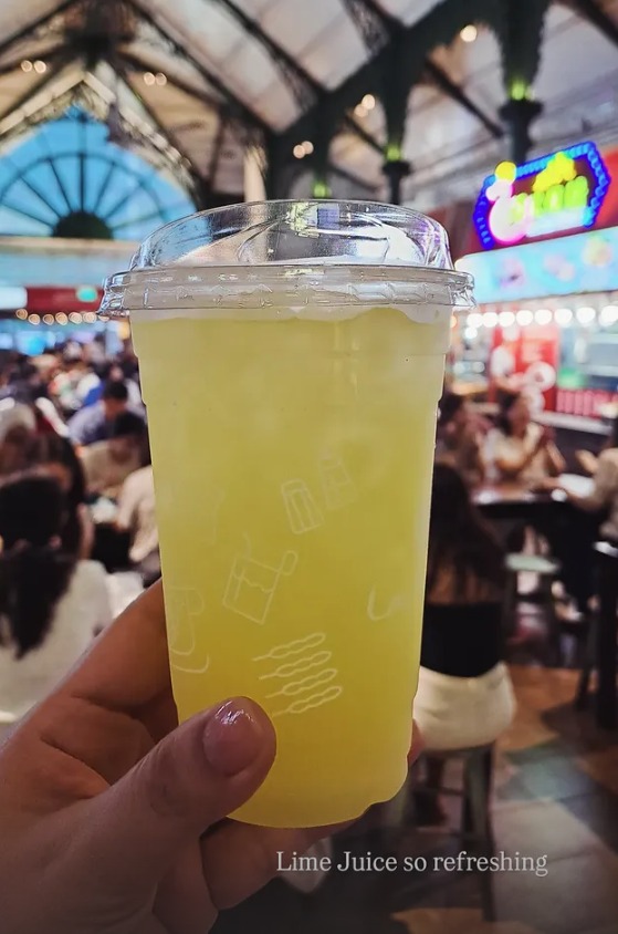 A cup of fresh lime juice held up in the hawker hall