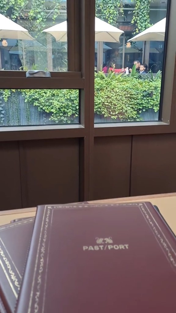 A Past/Port menu on a table by a window with greenery outside