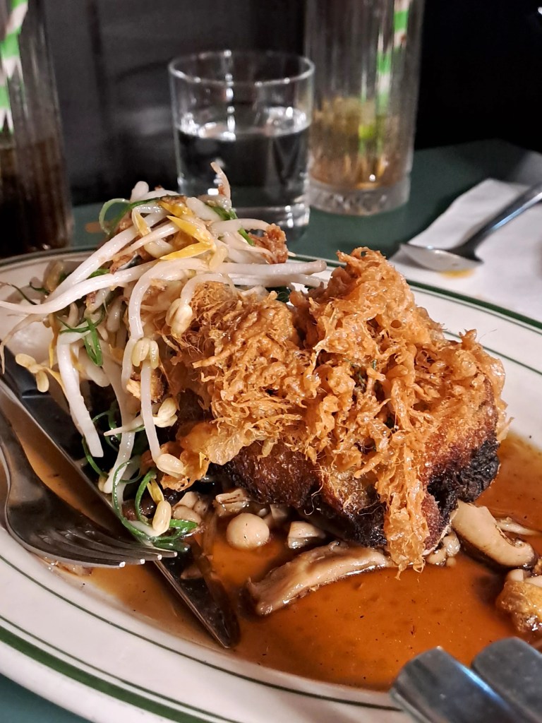 A dish topped with crispy floss on a bed of sprouts and sauce